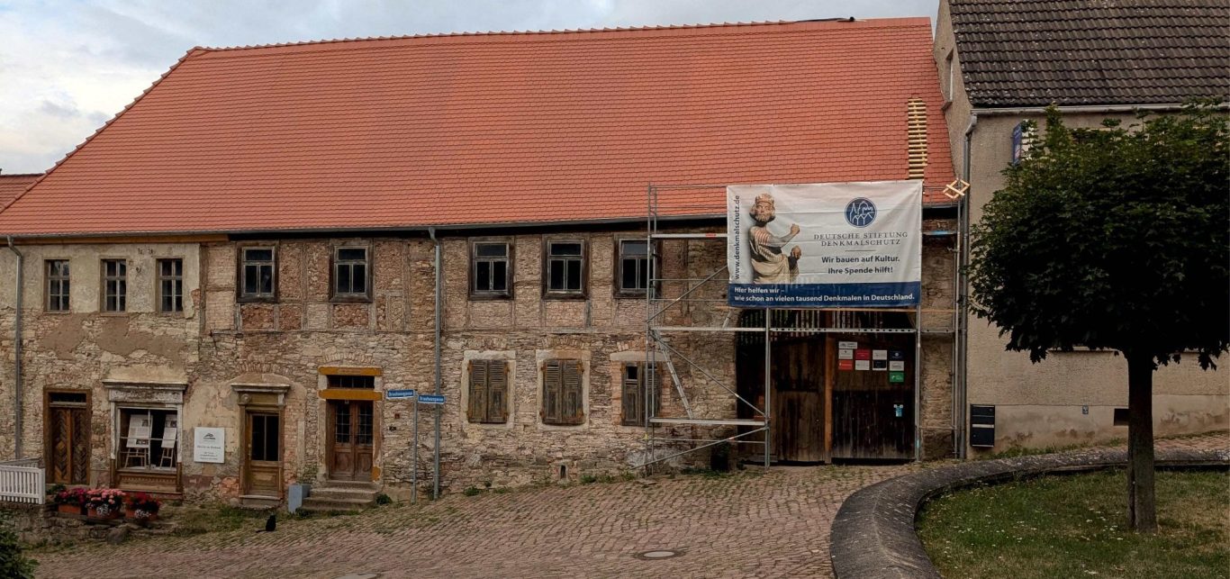 Einzeldenkmal Fassade eines alten, renovierungsbedürftigen Hauses mit Holzfenstern und rotem Dach.
