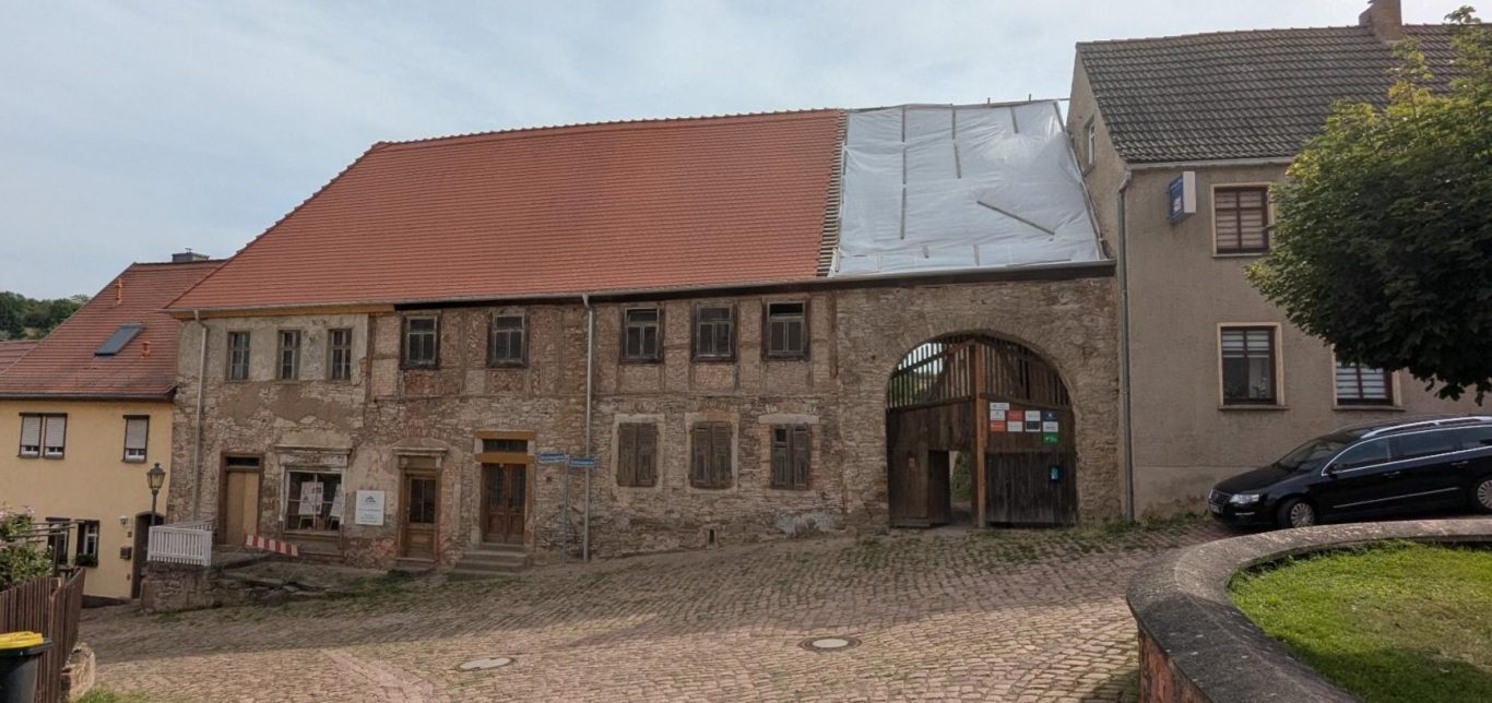 Einzeldenkmal Fassade eines alten, renovierungsbedürftigen Hauses mit Holzfenstern und rotem Dach.